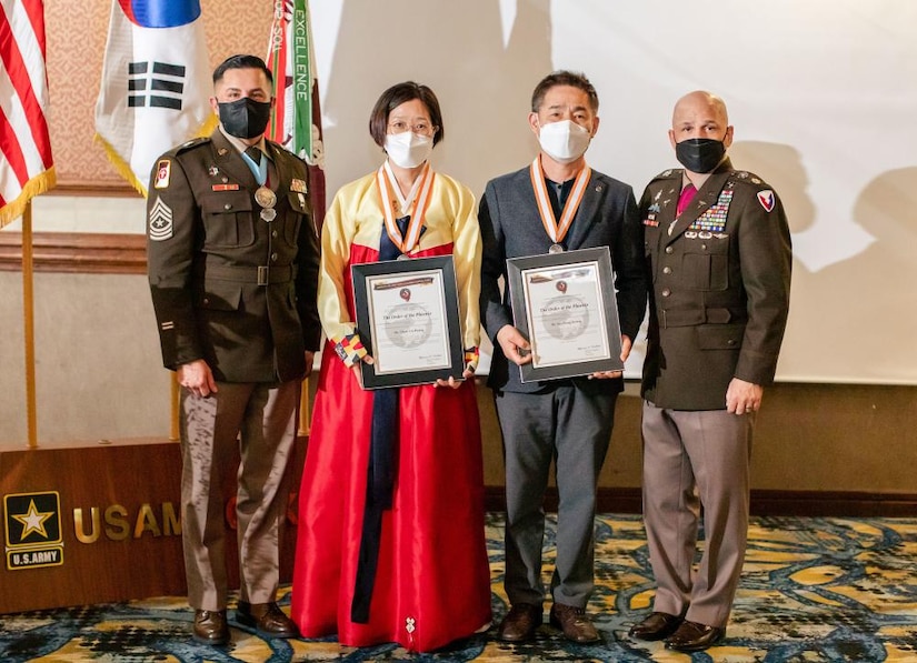 Lt. Col. Marcus D. Perkins, right, commander of the U.S. Army Medical Materiel Center-Korea, and Sgt. Maj. Joel Lara-Baeza, left, present its first Order of the Phoenix awards to Chon, Un-hyang, and So, Chang-kyong during the USAMMC-K staff appreciation dinner April 9. The Order of the Phoenix awards were created to recognize a lifetime of service to the medical materiel center. Not pictured is the third recipient, Choe, Song-kyu. (U.S. Army photo by Amy Gahan/Released)