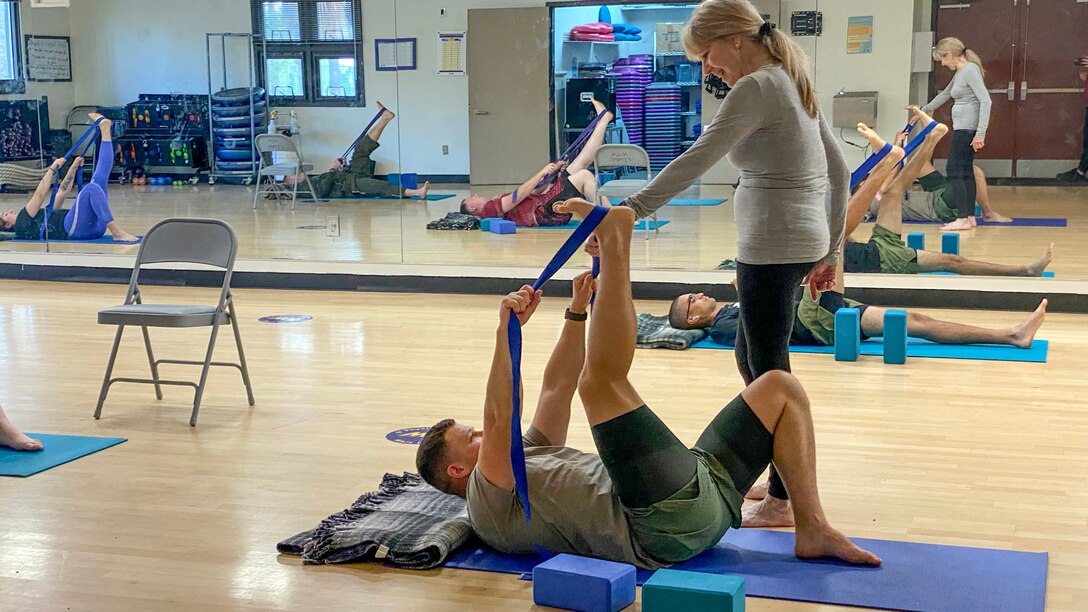 Instructor assists yoga student with stretching.