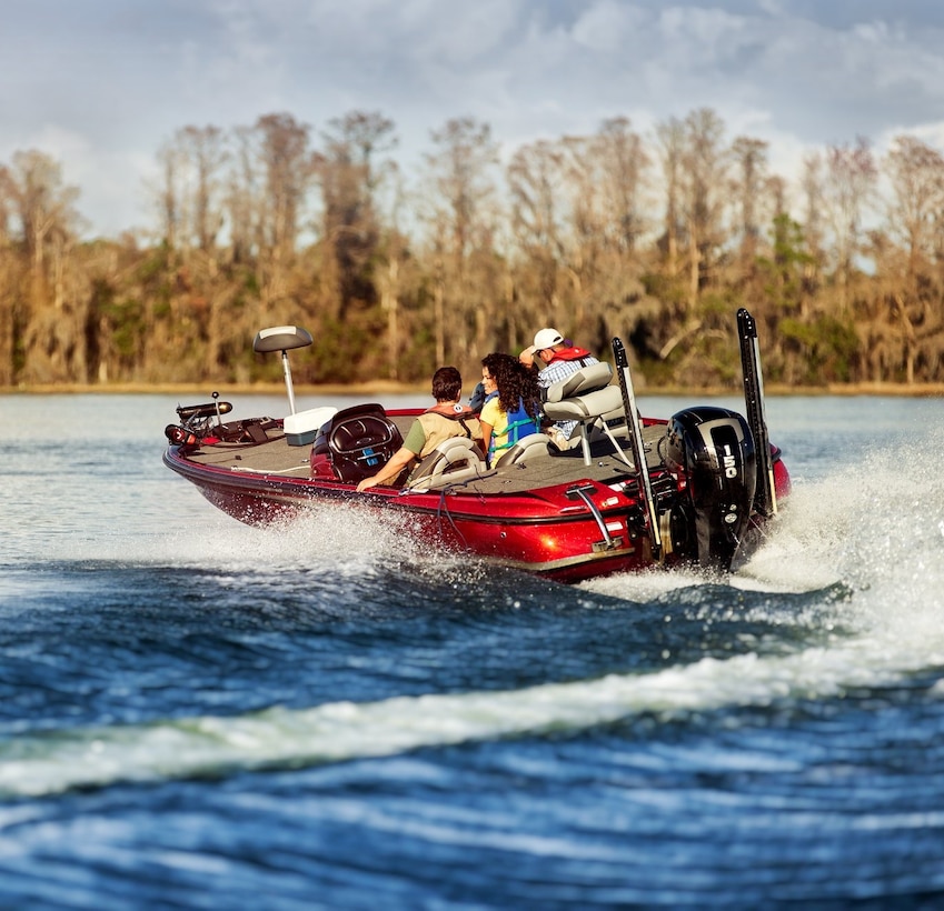 3 people wearing lifejackets on a red boat on a blue water lake with trees in the background.