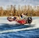 3 people wearing lifejackets on a red boat on a blue water lake with trees in the background.