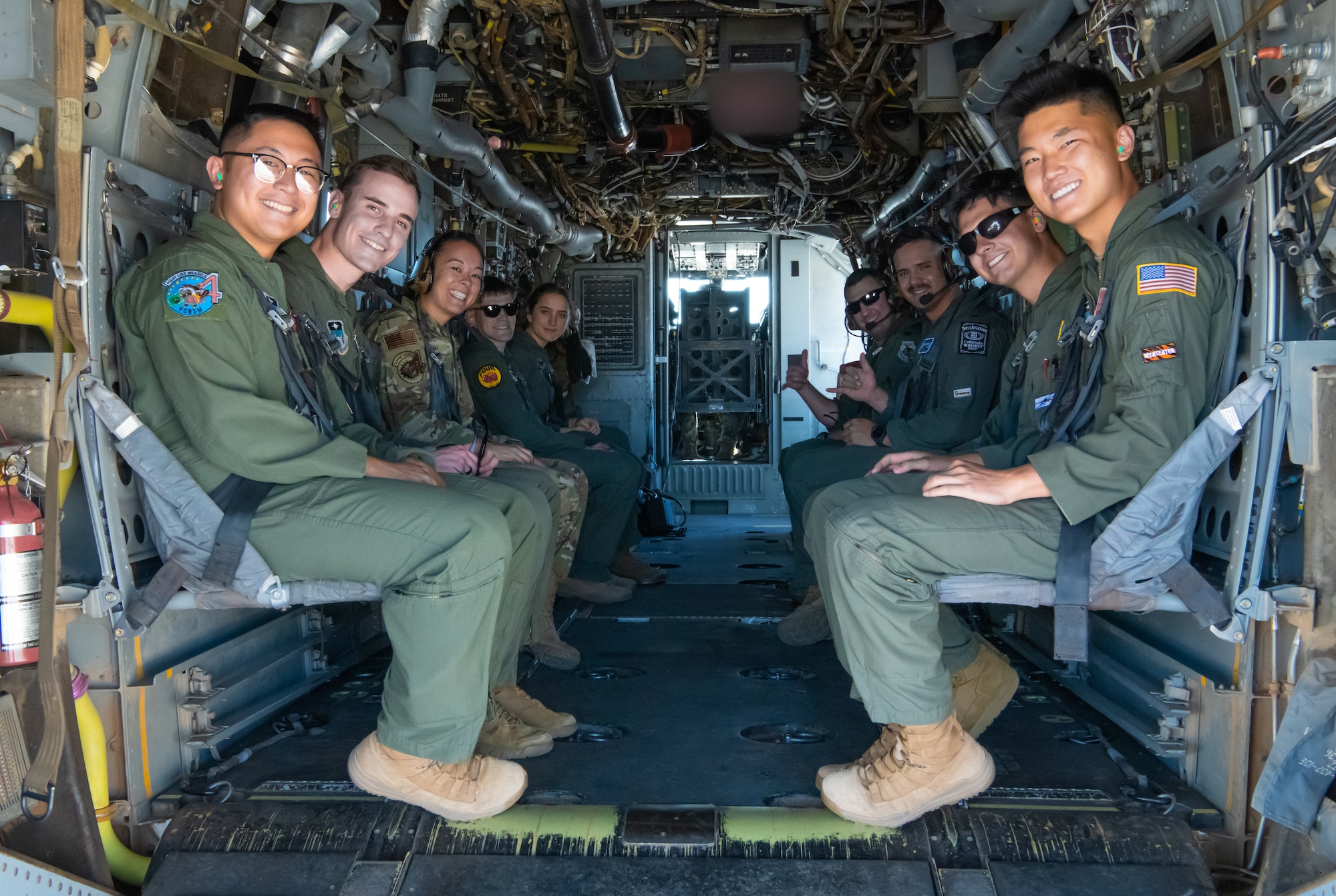 Airmen sitting in a military aircraft look towards out of the aircraft for a group photo.