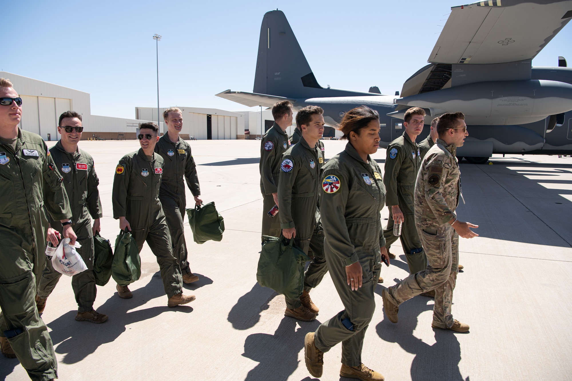 Airmen in camouflage uniforms and flight suits walk by a C-130 cargo airplane on a flight line.
