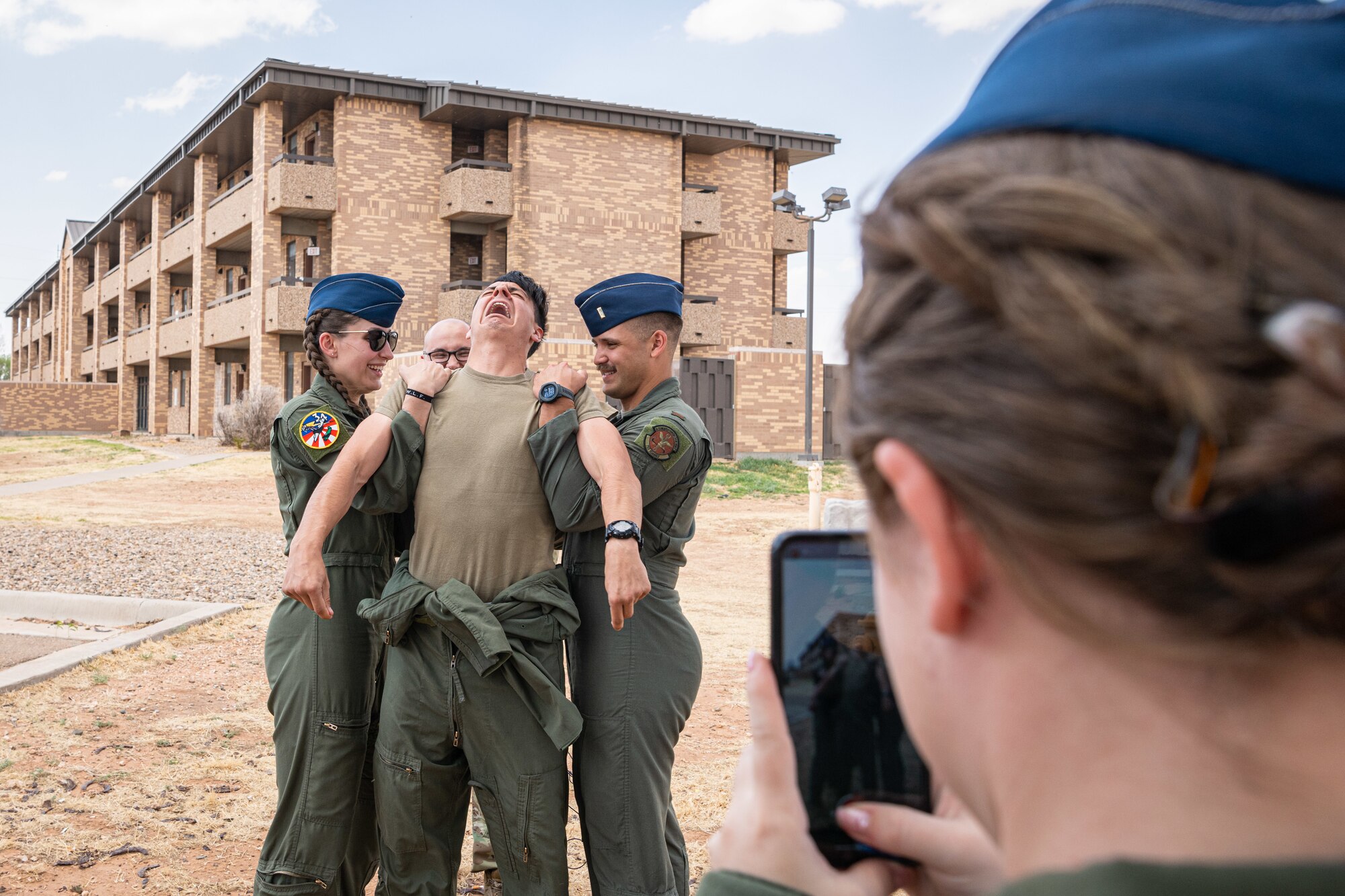 An Airman reacts as he is tased. Two other Airmen hold him to keep him from falling while another Airman films him with her phone.
