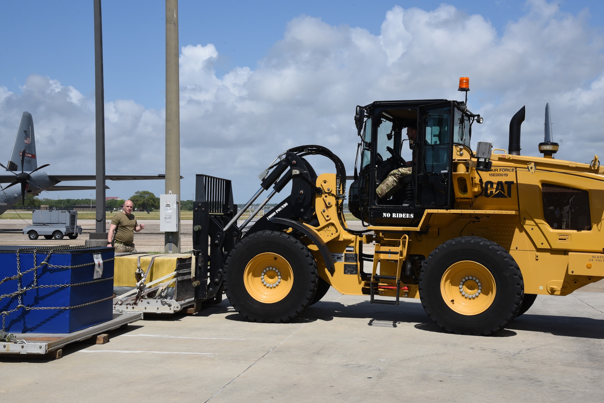 British Royal Air Force Reserve member marshals the driver of the all terrain 10K forklift, directing the placement of a pallet on beams on the ground.