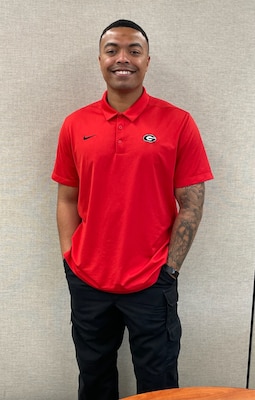 Man in red shirt, black pants standing against grey background