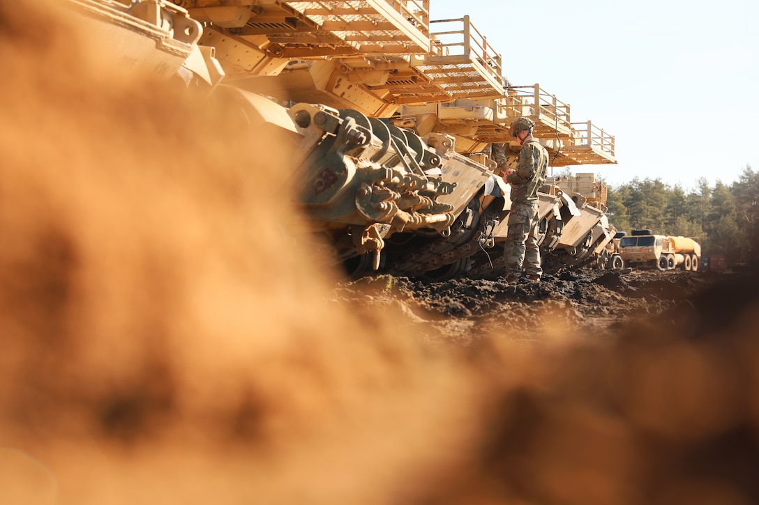 A soldier stands in front of a line of large vehicles.