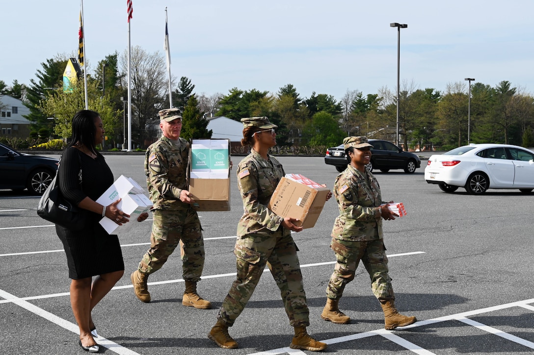 Three soldiers and a woman carry boxes as they walk across a parking lot.