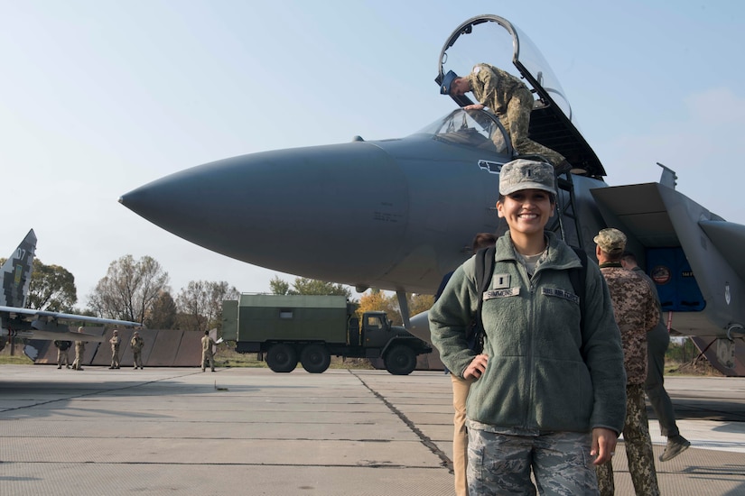An airman smiles for a photo in front of an aircraft on a flightline.