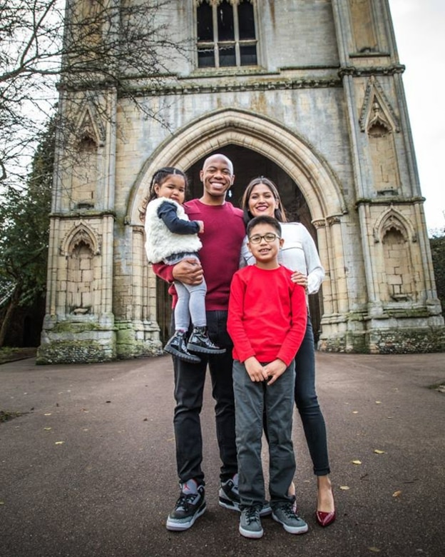 Two airmen in civilian clothes smile for a photo with two kids in front of an ornate Gothic-style building.