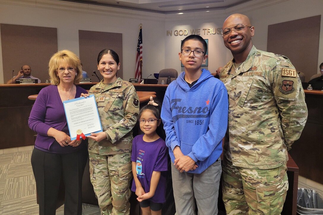 Two airmen stand for a photo with two kids and a civilian helping to hold up a document.