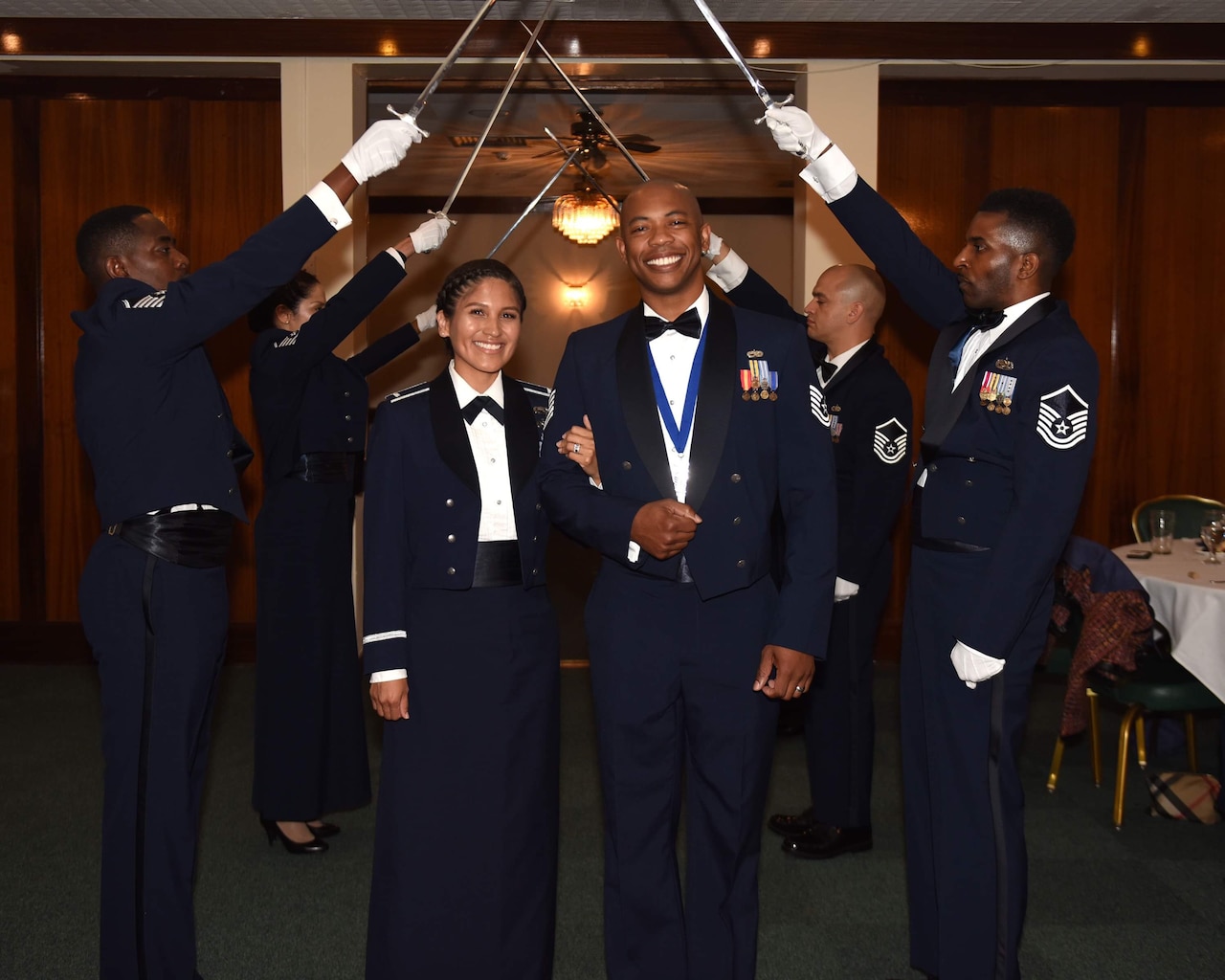 An Air Force couple smiles for a photo while walking under swords.