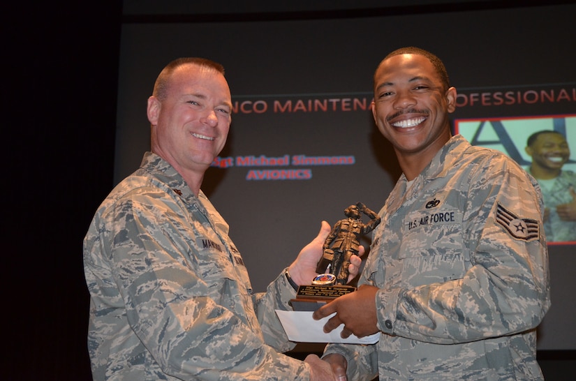 An airman smiles while accepting an award from another airman.