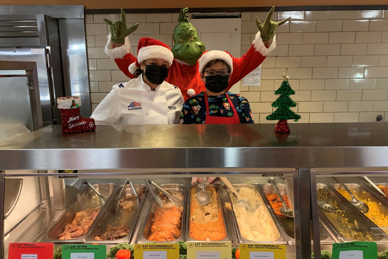 Three people are dressed in Christmas costumes behind a food counter.