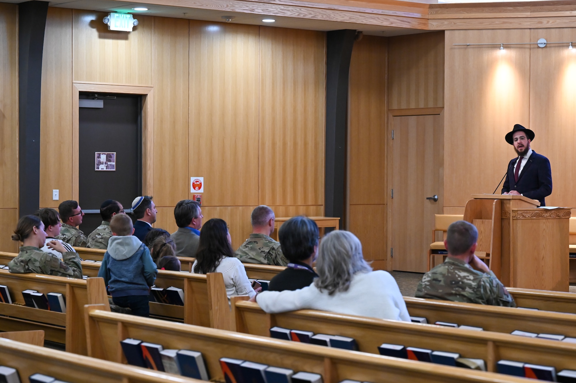 Rabbi Avremi Zippel speaks from behind a podium to audience members seated in pews.