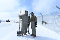 Two Airmen pose for a photo together on Minot Air Force Base, North Dakota, April 26, 2022. The Airmen were assisting in the shoveling of snow to create a trench to help water flow away from a missile launch facility. (U.S. Air Force photo by Senior Airman Caleb Kimmell)
