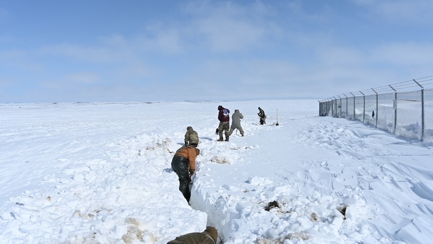 Airmen are shoveling snow April 26, 2022 on Minot Air Force Base, North Dakota. They are digging a trench to make sure the launch facility isn’t flooded by the melting snow. (U.S. Air Force photo by Senior Airman Caleb Kimmell)