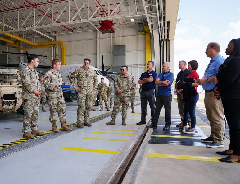 Civic leaders and Airmen stand in a hangar and talk. Aircraft are on display in the hangar.