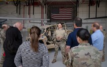A group of civic leaders stand in a hangar and listen to a briefing  by a 919th Special Operations Security Forces Squadron. An MRZR combat vehicle and American flag are in the background.