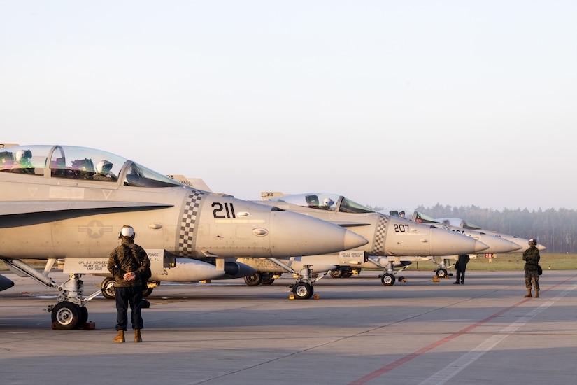 Marines stand beside jets on a flightline.