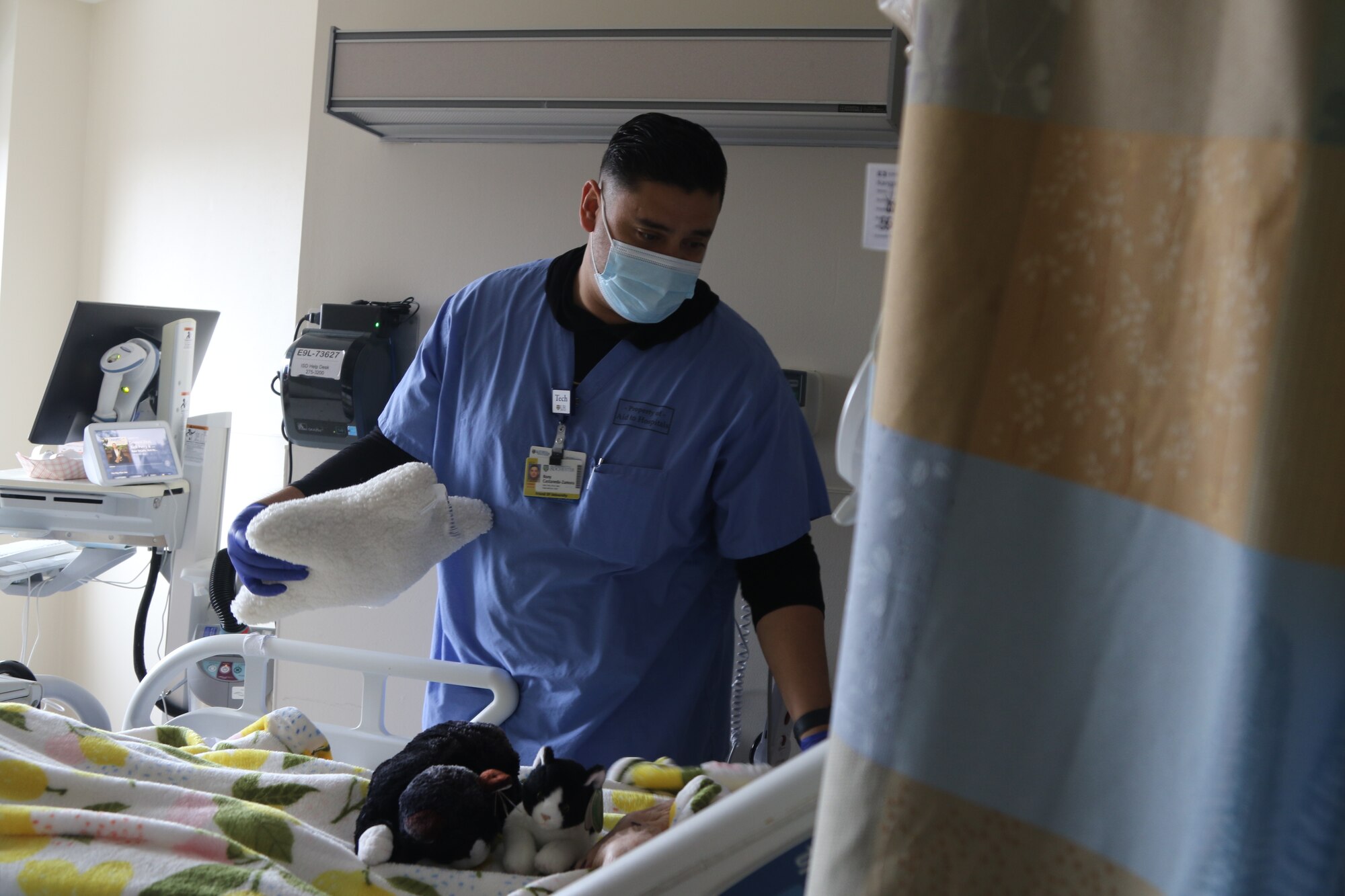 U.S. Air Force Tech Sgt. Rony Castaneda-Zamora, a medical technician assigned to a military medical team, hands a patient their pillow while supporting the COVID response operations at University of Rochester Medical Center, Rochester, New York, March 5, 2022.