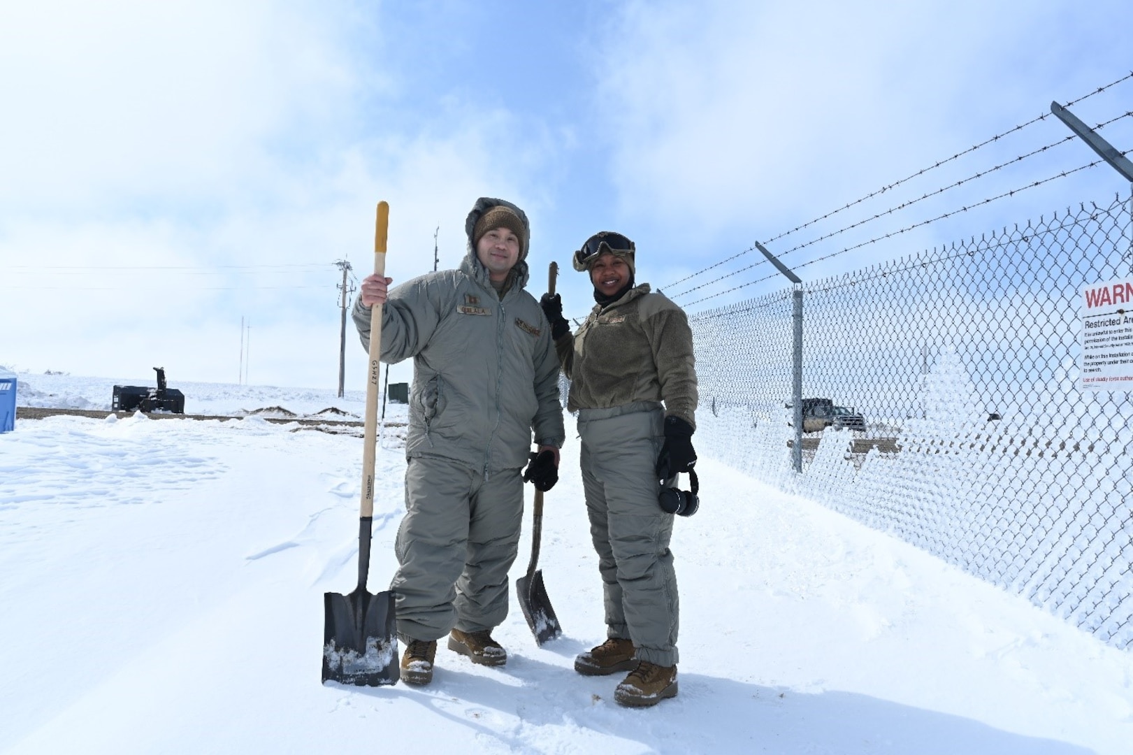 Two Airmen pose for a photo together on Minot Air Force Base, North Dakota, April 26, 2022. The Airmen were assisting in the shoveling of snow to create a trench to help water flow away from a missile launch facility. (U.S. Air Force photo by Senior Airman Caleb Kimmell)