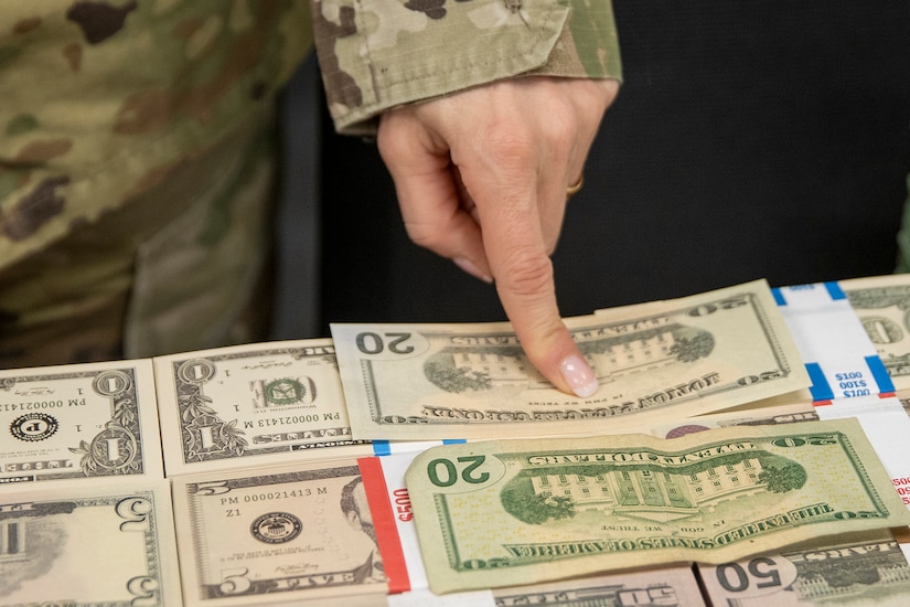 Col. Paige M. Jennings, U.S. Army Financial Management Command commander, compares new Operational Training Team training currency against real U.S. currency in the OST’s storage room at the Maj. Gen. Emmett J. Bean Federal Center in Indianapolis April 8, 2022. The very few differences between real U.S. dollars and the new fake ones are a few markings and phrases integrated into the training currency, making training more realistic. (U.S. Army photo by Mark R. W. Orders-Woempner)