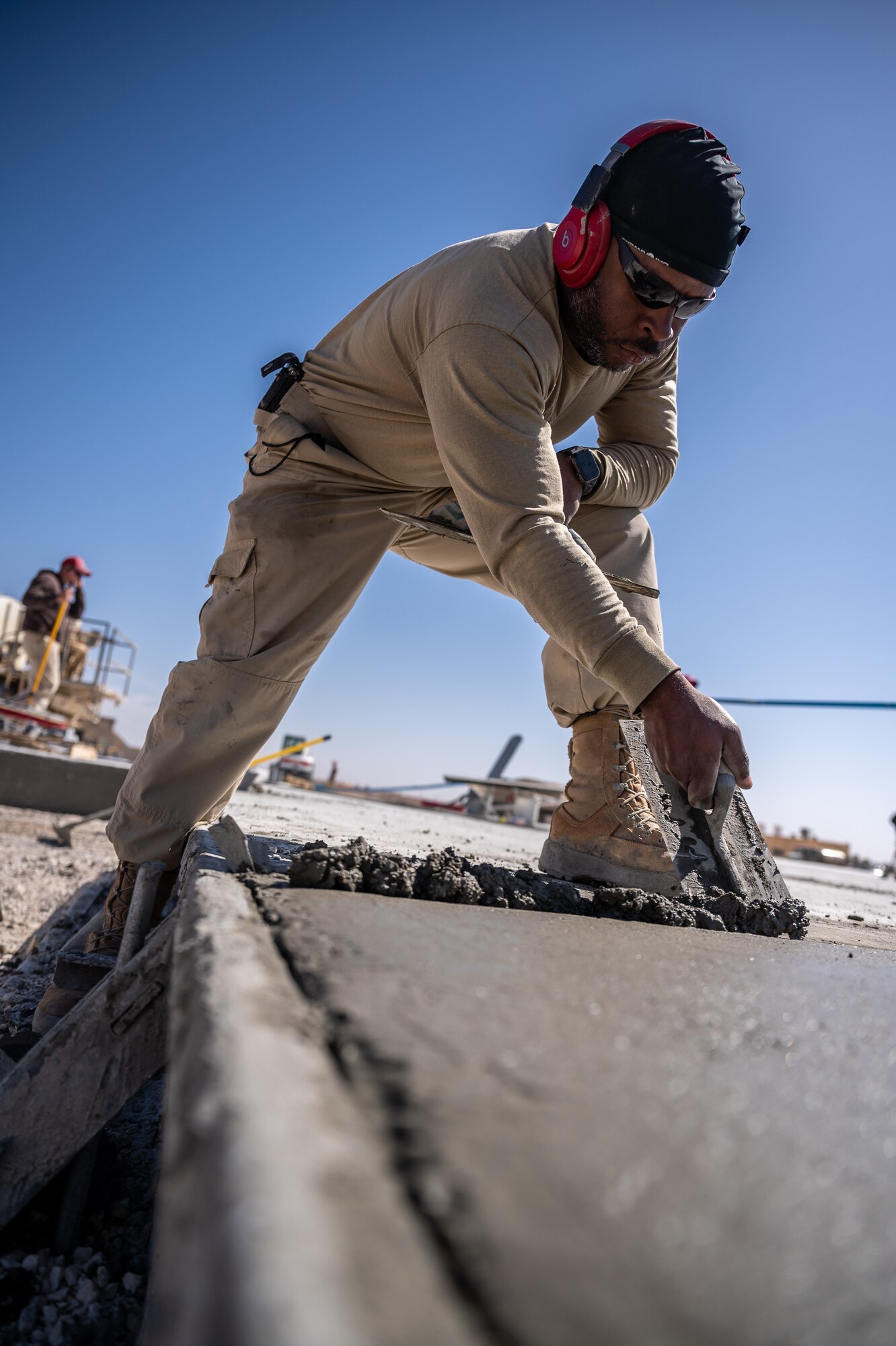 Tech. Sgt. Nolan Denson, 1st Expeditionary Civil Engineer Group pavements and construction equipment operator craftsman, adds concrete to a low spot in poured concrete during a runway overrun repair project at an undisclosed location in Southwest Asia, April 14, 2022. (U.S. Air Force photo by Master Sgt. Christopher Parr)