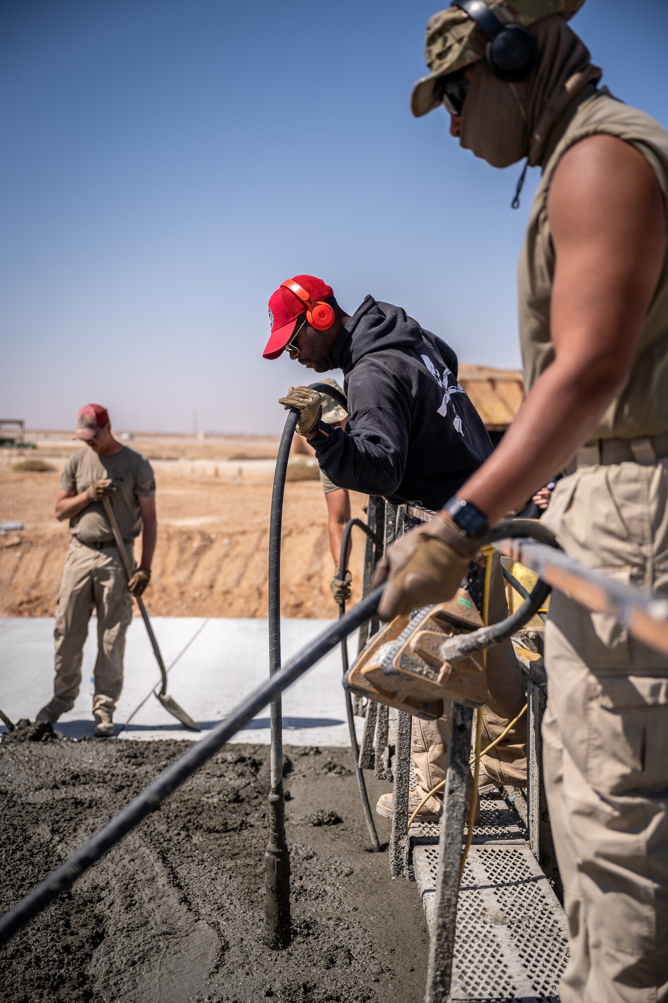 Tech. Sgt. Meshach Barker and Tech. Sgt. Max Silva, 1st Expeditionary Civil Engineer Group pavements and construction equipment operator craftsmen, stand on a roller screed to vibrate concrete as it is placed during a runway overrun repair project at an undisclosed location in Southwest Asia, April 14, 2022. Vibrating concrete consolidates and eliminates air pockets present in a freshly poured concrete pad. (U.S. Air Force photo by Master Sgt. Christopher Parr)