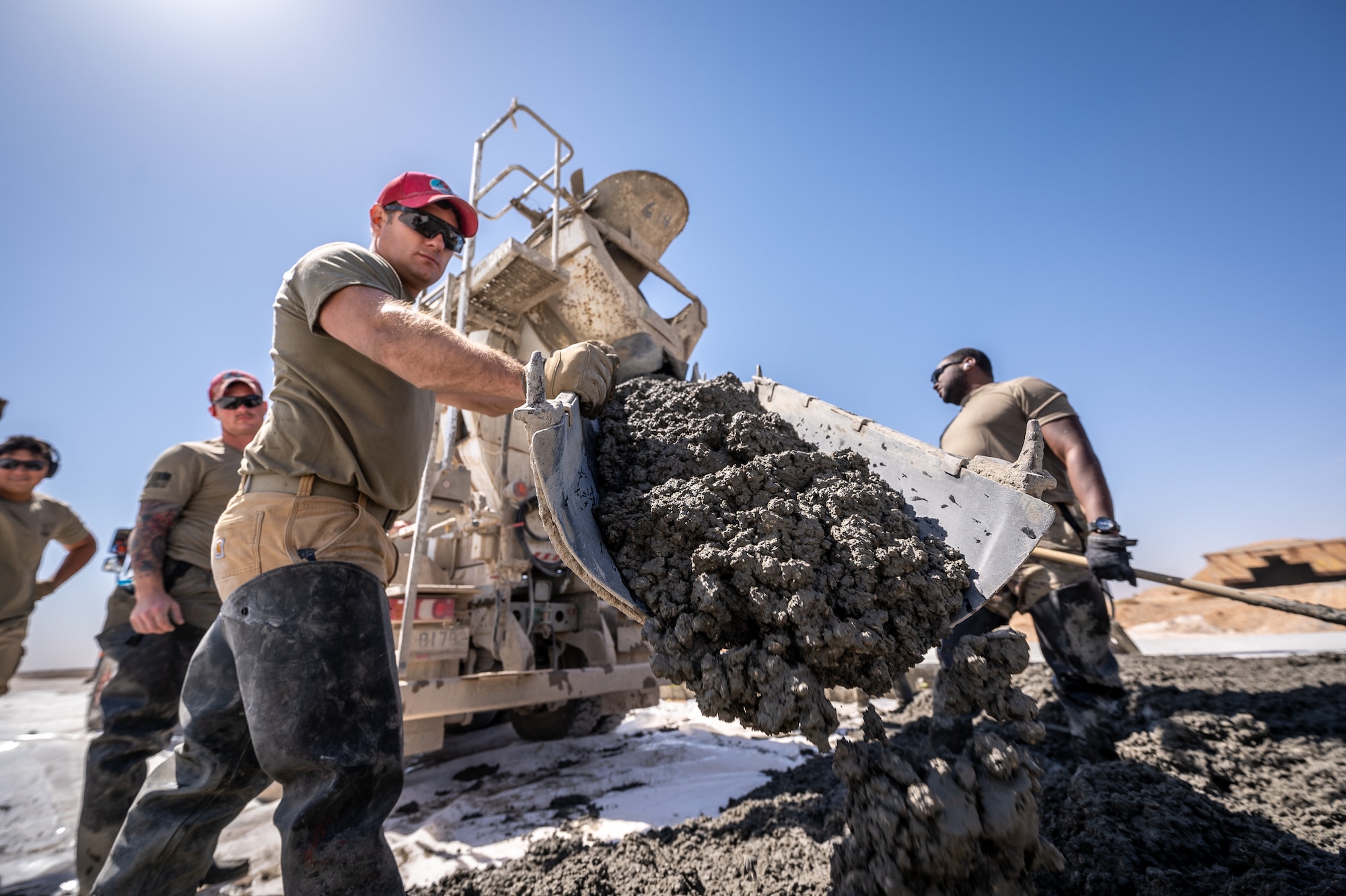 Tech. Sgt. Ryan Speicher, 1st Expeditionary Civil Engineer Group lead chute operator, spreads concrete from a cement truck during a runway overrun repair project at an undisclosed location in Southwest Asia, April 14, 2022. Evenly spread concrete aids in preventing major high or low spots during the pour. (U.S. Air Force photo by Master Sgt. Christopher Parr)