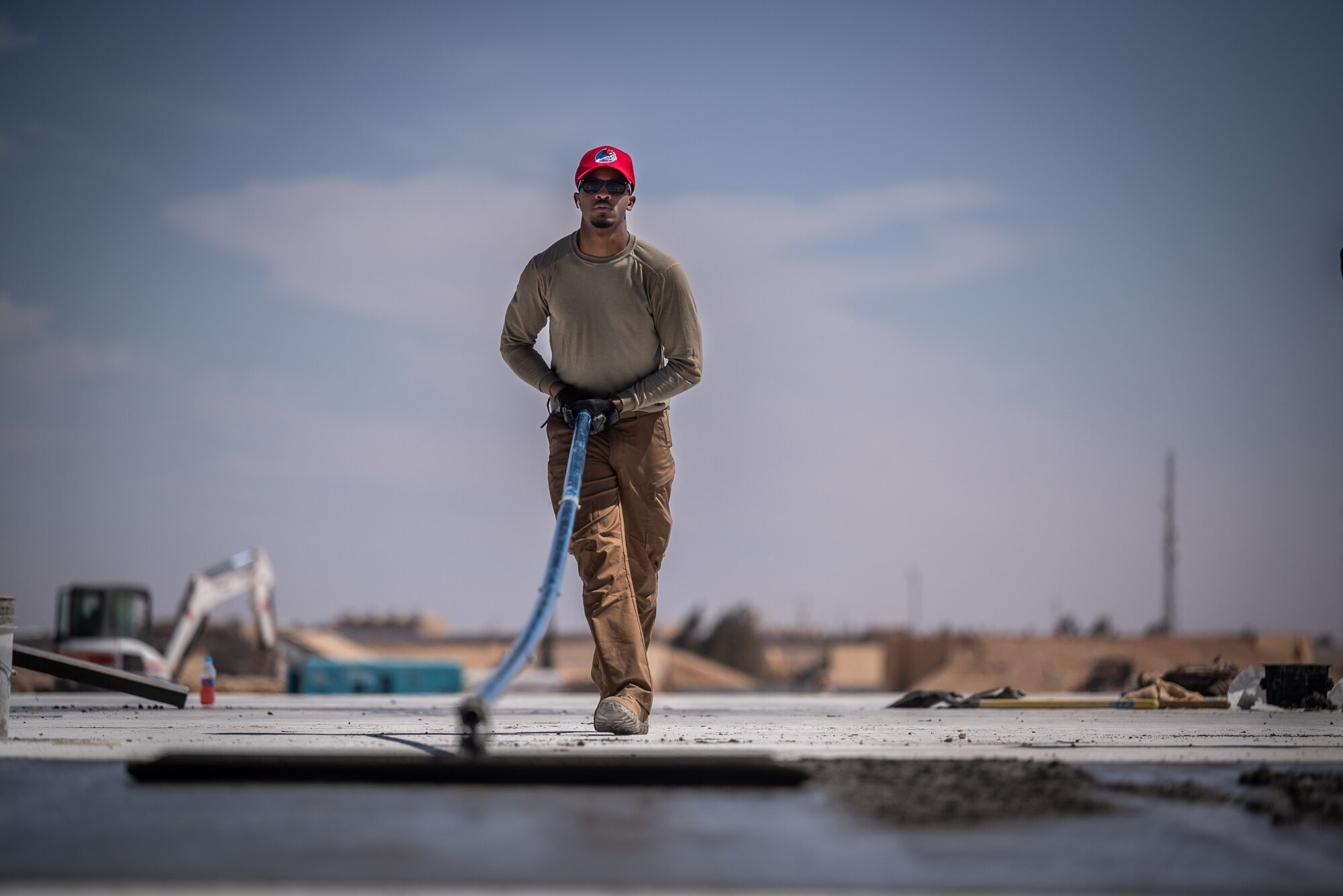 Airman First Class Jan Quenado, 1st Expeditionary Civil Engineer Group pavements and construction equipment operator journeyman, uses a bull float to eliminate uneven areas left by the roller screed during a runway overrun repair project at an undisclosed location in Southwest Asia, April 14, 2022 (U.S. Air Force photo by Master Sgt. Christopher Parr)