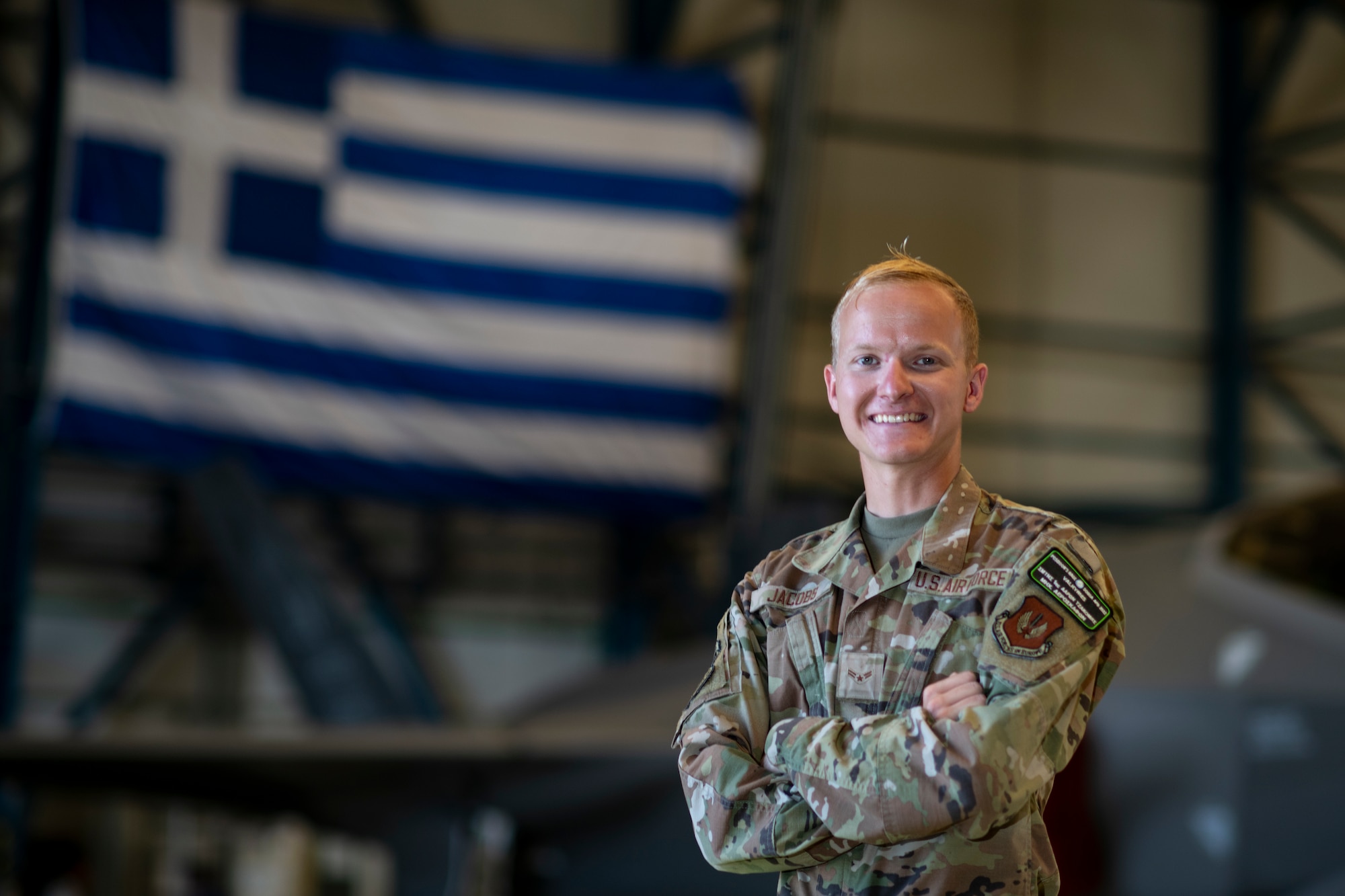 An Airman standing in front of a jet and the Greek flag