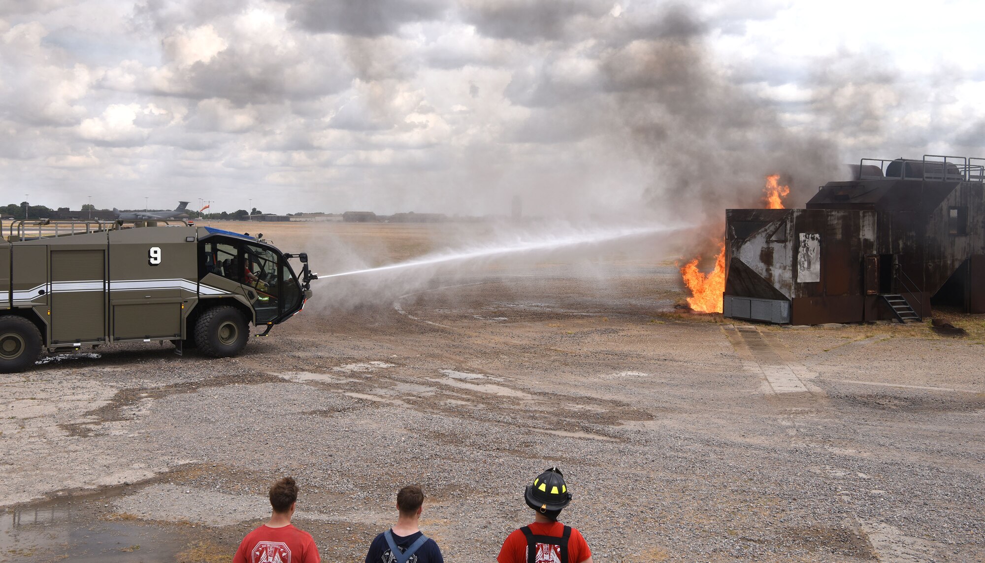 Water is shot from a P-19 Panther aircraft rescue and firefighting crash truck onto flames of a simulated aircraft at the live-fire training area on Royal Air Force Mildenhall, England, July 28, 2022. U.S. Air Force Col. Gene Jacobus, 100th Air Refueling Wing commander, rode in the truck and had the opportunity to do live-fire training to learn what goes on behind the scenes to protect the base and mission every day. (U.S. Air Force photo by Karen Abeyasekere)