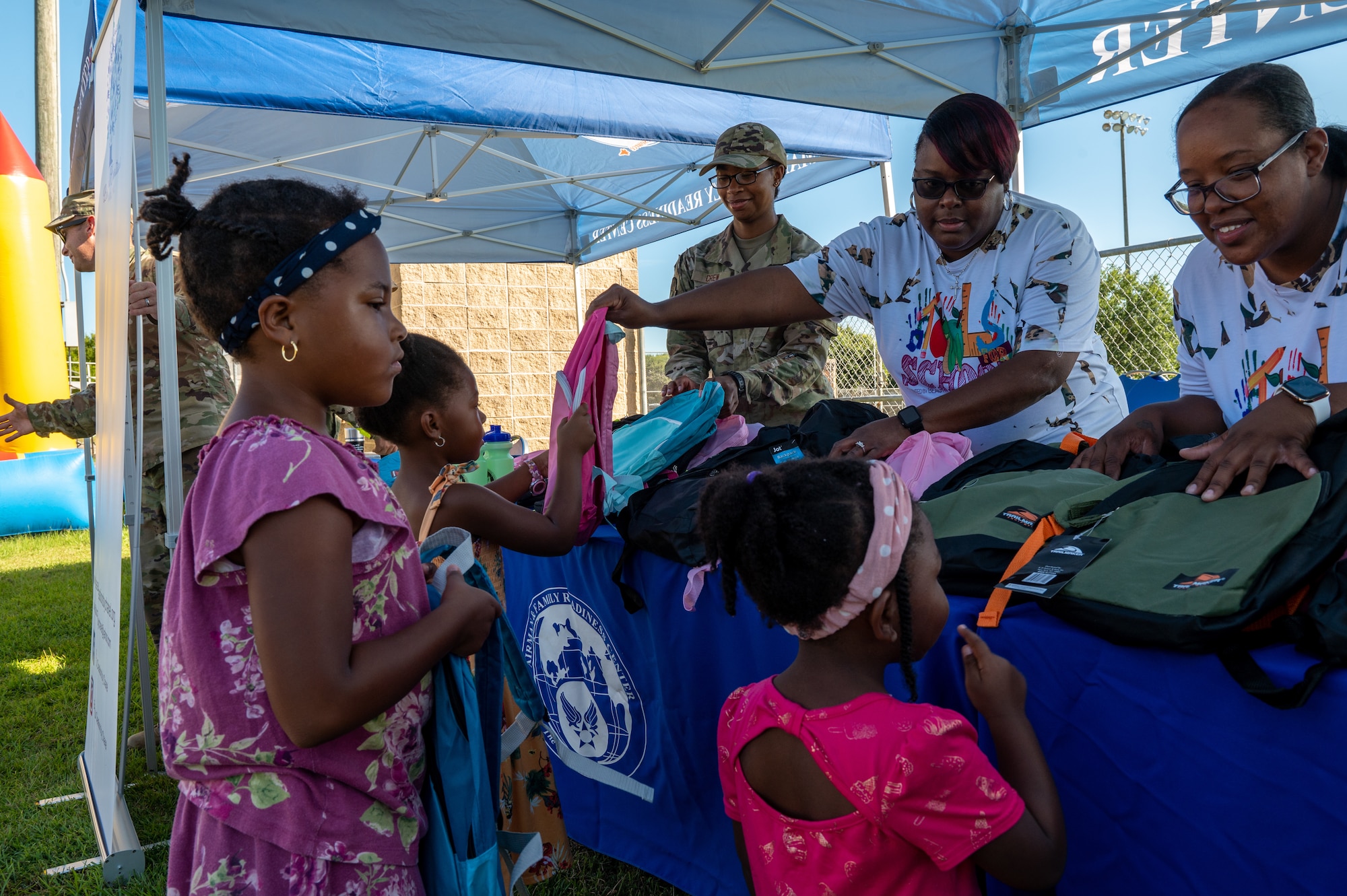 Children select a backpack from a table of school supplies during a back to school field day event.