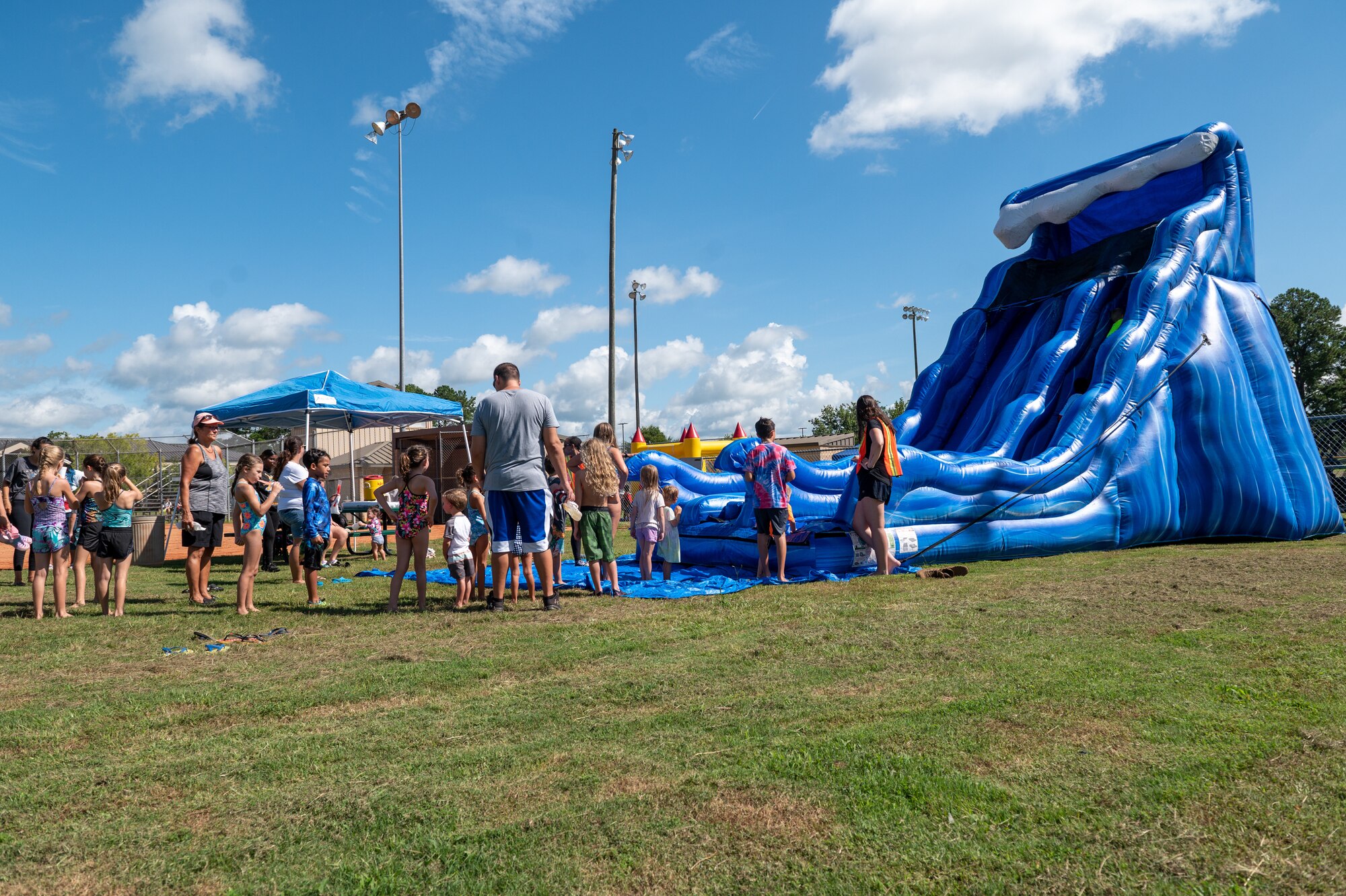 Military families wait in line to go down and inflatable water slide during an outdoor field day.