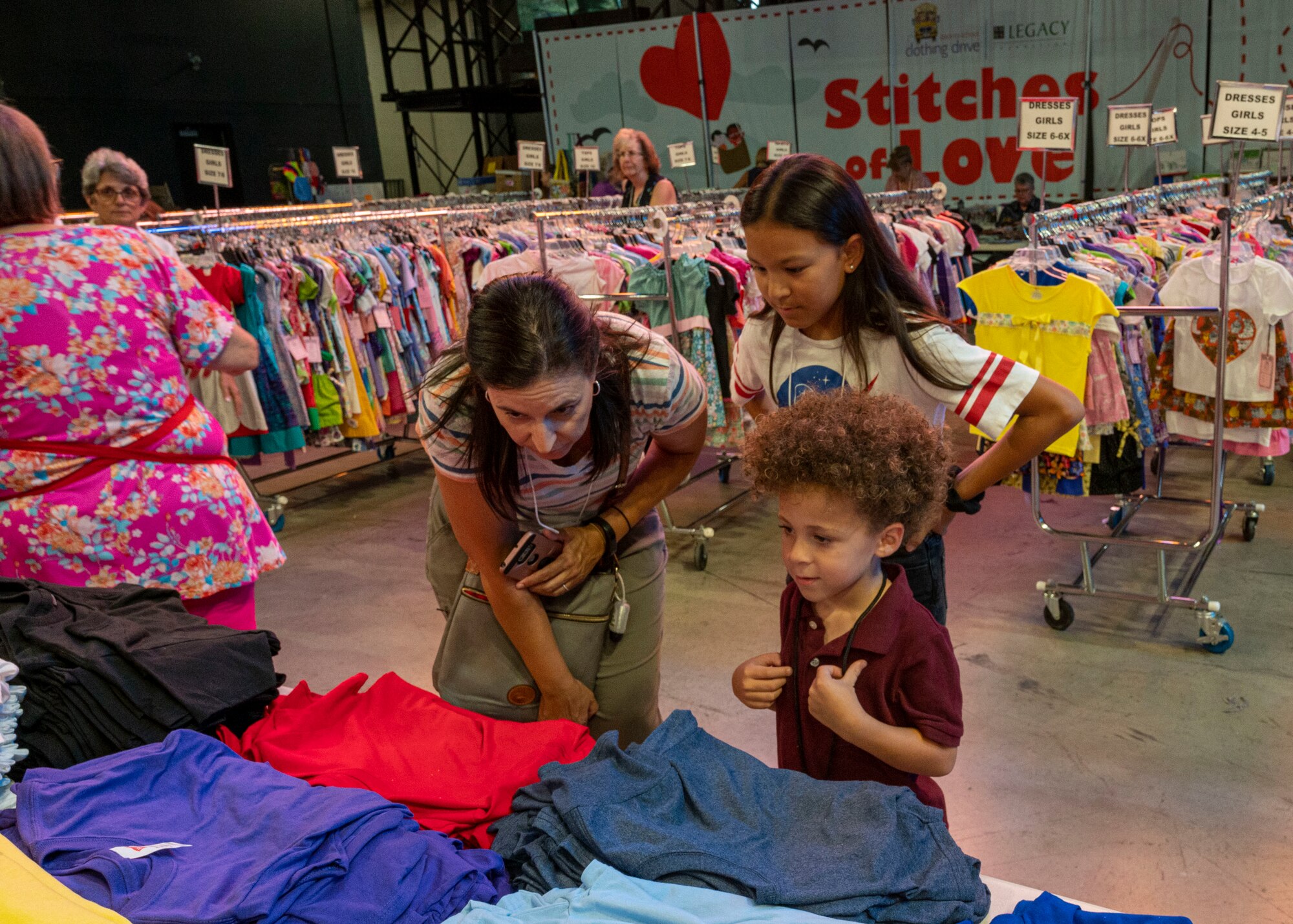 A volunteer helps two children pick out clothes from the “Stitches of Love” program at the Back to School Bash event July 20, 2022, at Grand Canyon University, Phoenix, Arizona.
