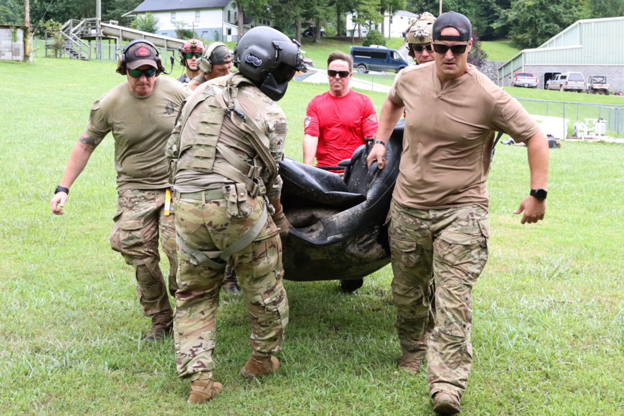 Soldiers carry an inflatable raft in a field.