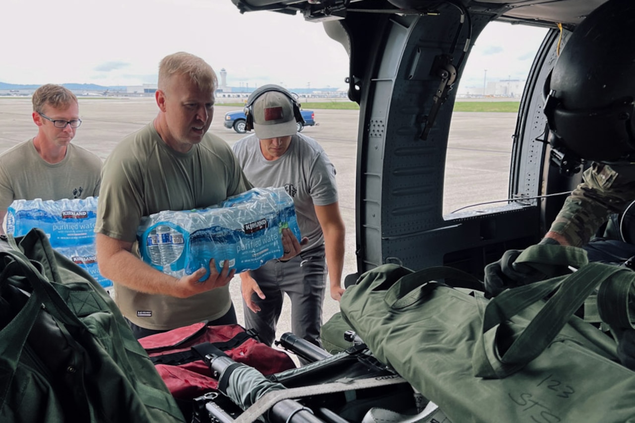 Soldiers carry cases of bottled water to the open door of a parked helicopter.