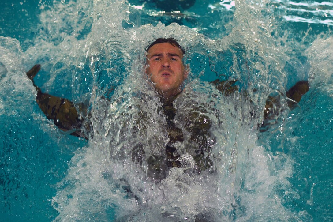 A soldier swims on his back in a pool.