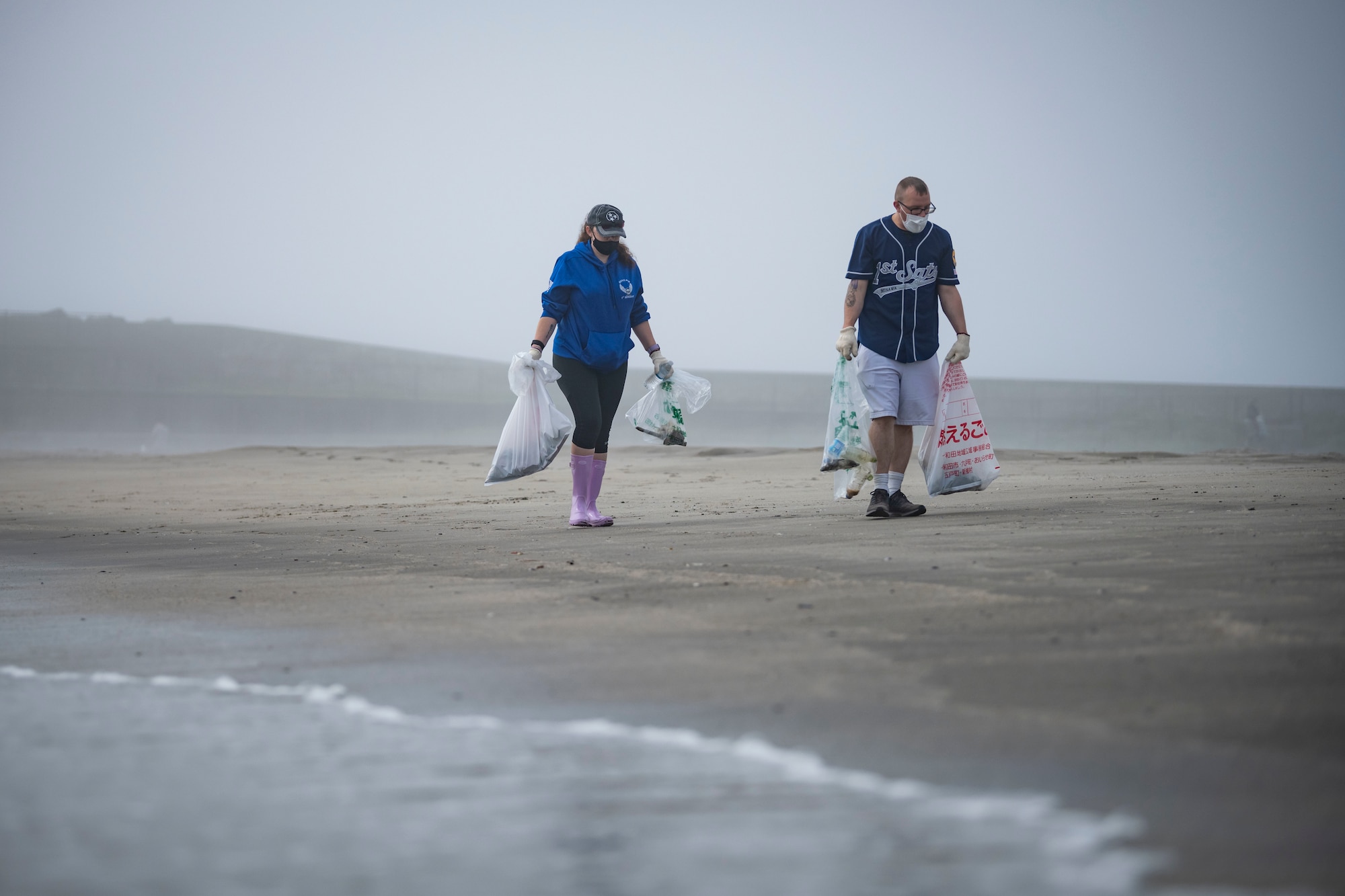 Team Misawa members hold garbage bags as they walk next to waves crashing.