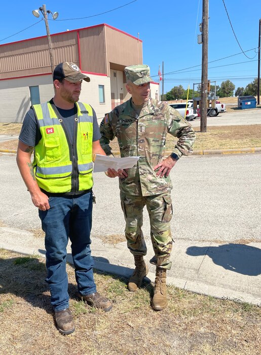 Two people in construction safety equipment walk and talk next to eachother