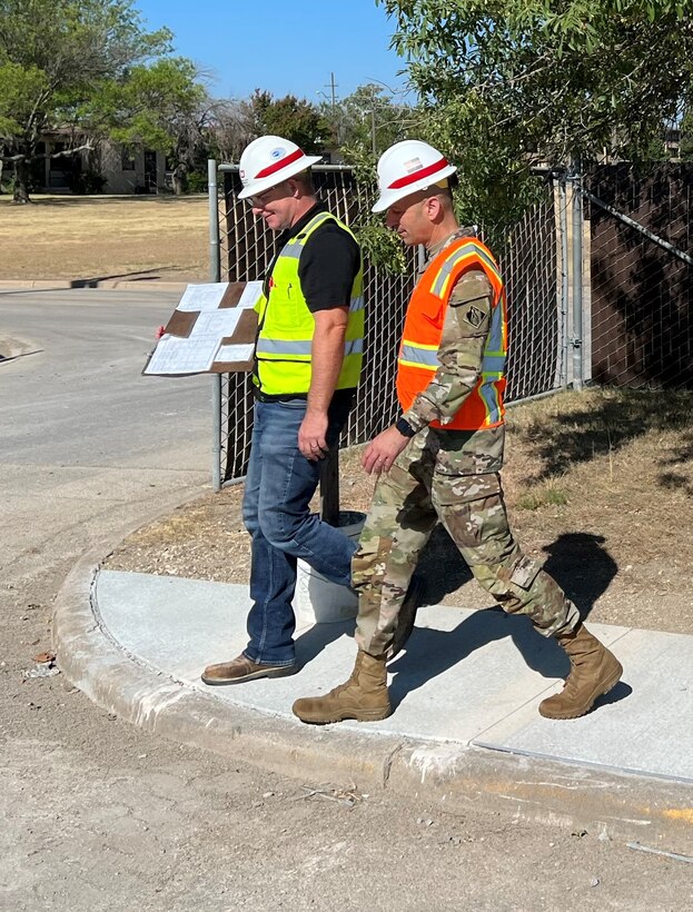 Two people in construction safety equipment walk and talk next to eachother