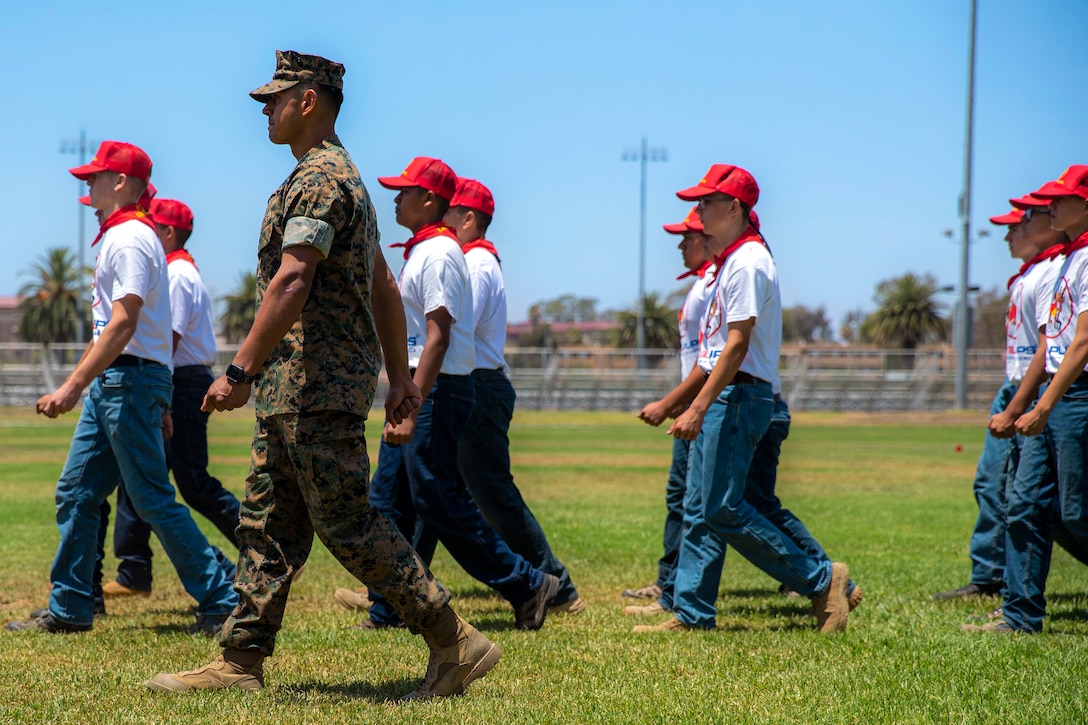 A group of young students march with a Marine.