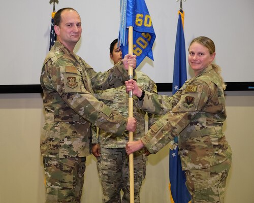 photo of two USAF Airmen holding unit flag with another USAF Airman standing at attention in the background