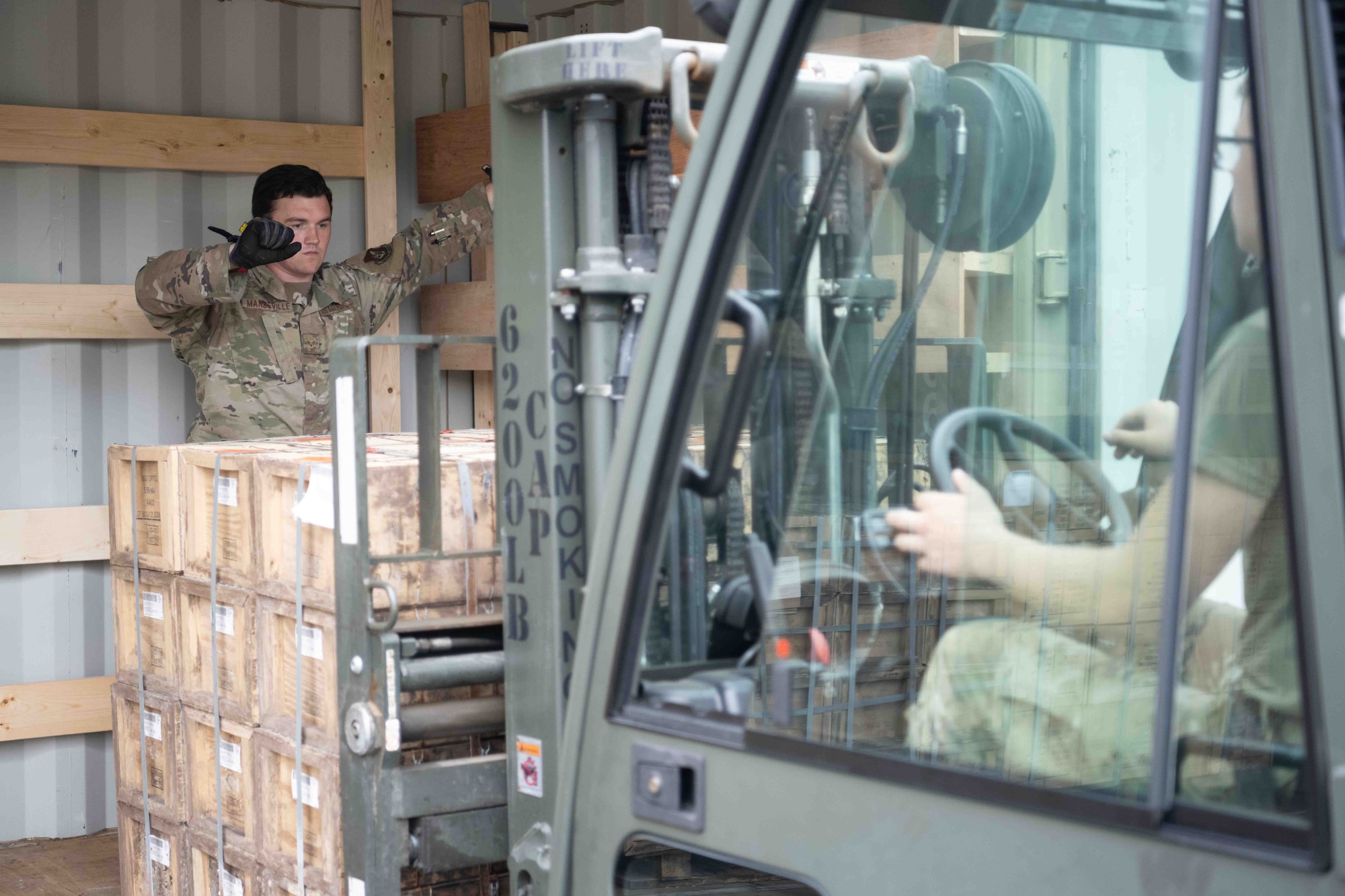 A military member guids another operating a forklift.