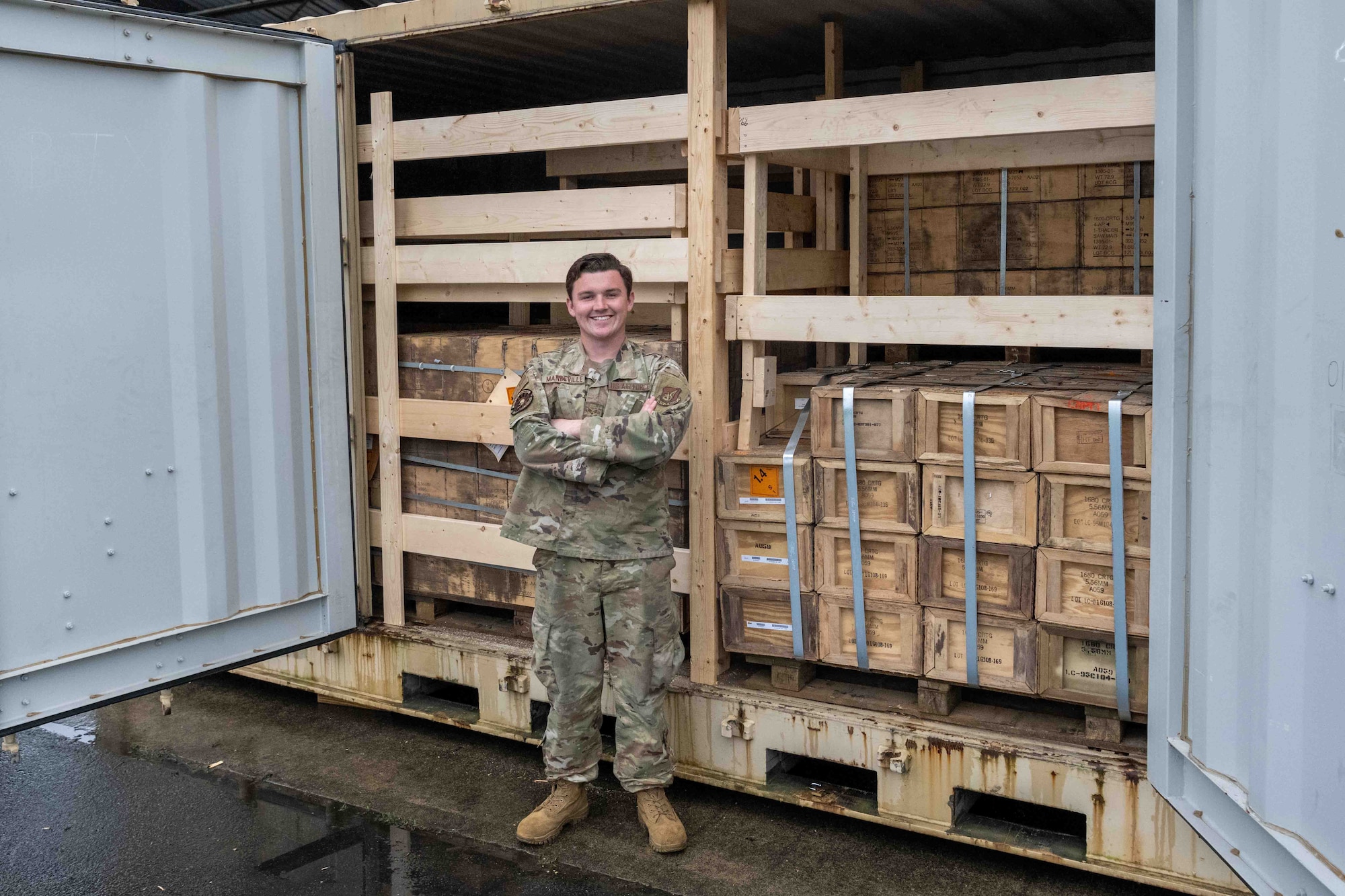 A military member stands in front of a filled shipping crate.