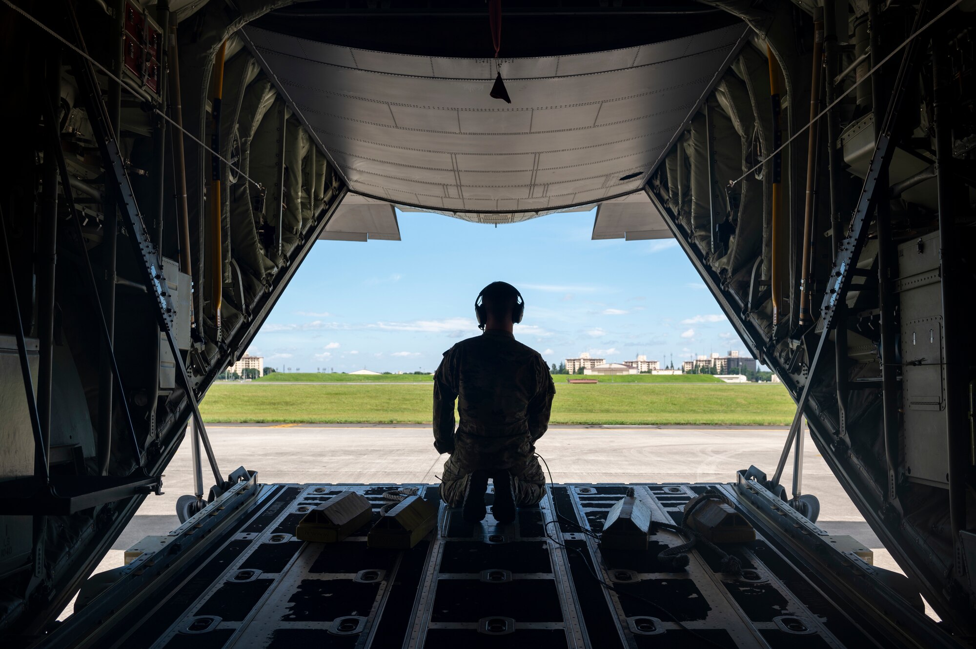 I loadmaster sits in silhouette as he looks out the back of a plan's rear hatch