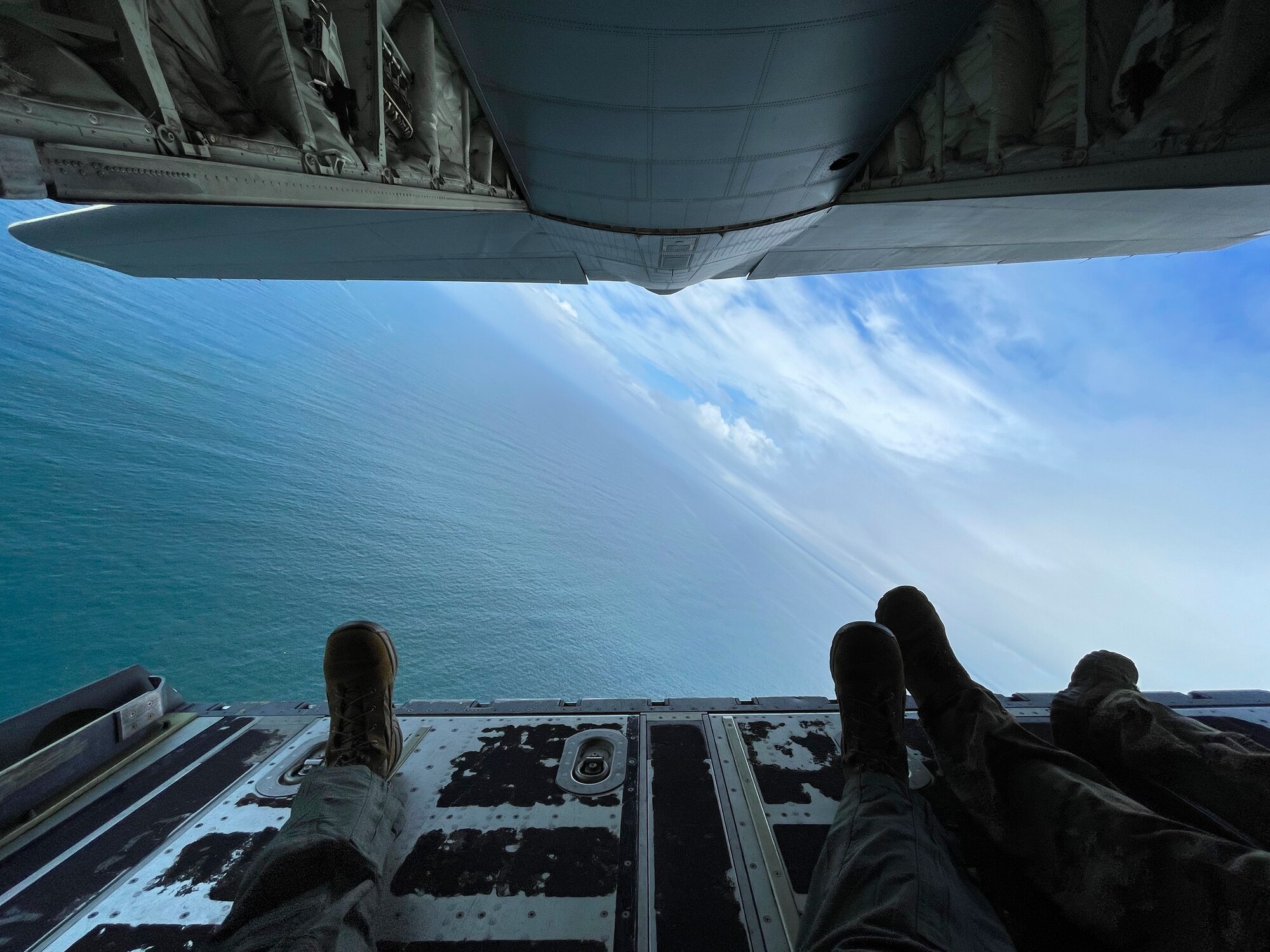 Feet dangle out the back of an aircraft flying over the open ocean