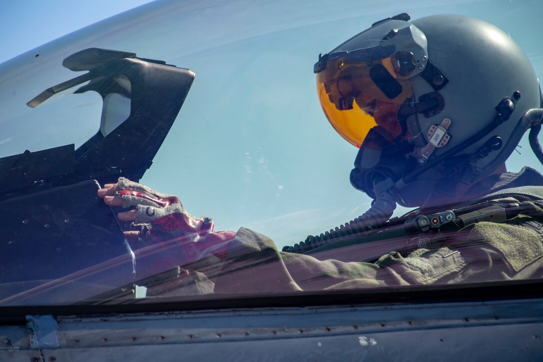 A pilot wears a flight helmet with an equipped oxygen mask and sits in the cockpit of a jet.