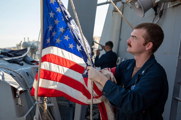 Quartermaster 1st Class Andrew Masino, from Jacksonville, Florida, shifts colors aboard the Arleigh Burke-class guided-missile destroyer USS Bainbridge (DDG 96) during a scheduled port visit to Civitavecchia, Italy, Aug. 2, 2022. Bainbridge is on a scheduled deployment in the U.S. Naval Forces Europe area of operations, employed by U.S. Sixth Fleet to defend U.S., allied and partner interests.