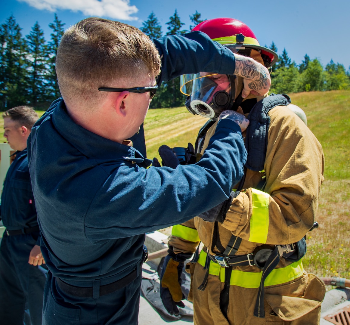 Information Services Technician First Class Mason Foreman, USS Connecticut (SSN 22), helps a shipmate don firefighting gear and performs essential safety checks on his mask, a self-contained breathing apparatus worn during fire fighting. (U.S. Navy Photo by Wendy Hallmark)